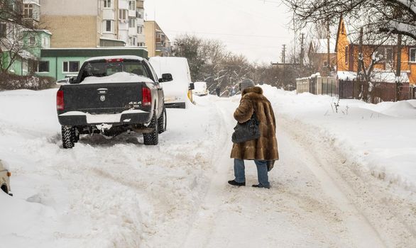Lutsk, Ukraine - February 12,2020: Uncleaned slippery roads and sidewalk in winter. Cars in snowdrift. People on street after snow storm. City street after blizzard. Record-breaking amounts of snow