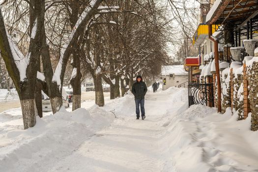 Lutsk, Ukraine - February 12,2020: People on street after snow storm. City street after blizzard. Record-breaking amounts of snow. Uncleaned slippery roads and sidewalk in winter. Cars in snowdrift