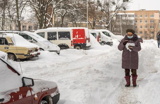 Lutsk, Ukraine - February 12,2020: City street after blizzard. Record-breaking amounts of snow. Health protection. Woman wearing face mask on public street in middle of coronavirus epidemic in winter