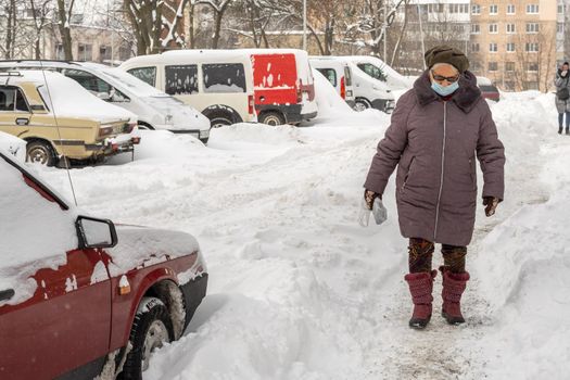 Lutsk, Ukraine - February 12,2020: City street after blizzard. Record-breaking amounts of snow. Health protection. Woman wearing face mask on public street in middle of coronavirus epidemic in winter