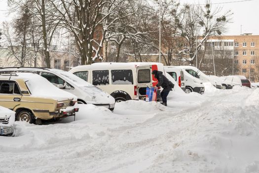 Lutsk, Ukraine - February 12,2020: Stuck car in snow and ice. City street after blizzard. Buried vehicle in snowdrift. Parking in winter after snowfall. Uncleaned road. Record-breaking amounts of snow