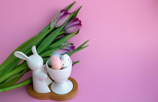 White rabbit, Easter eggs and lilac tulips on pink background, Easter celebration concept.