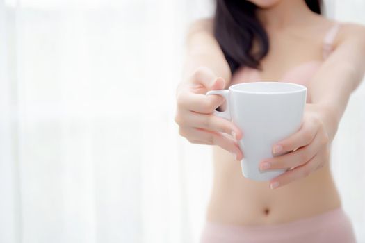 Closeup young asian sexy woman in underwear giving coffee near windows in the morning, girl with seductive figure fit serving beverage is breakfast for relax after wake up, lifestyle concept.