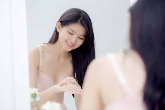 Beautiful sexy young asian woman looking mirror applying cream on hand and message, beauty girl applying body lotion skin care for health and soft hydration, treatment and cosmetic with moisturizer.