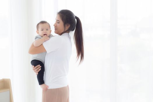 Young asian mother holding little baby girl and walking together in the bedroom at home, mom carry daughter and care, relationship of parent and child, toddler and parent, indoor, family concept.