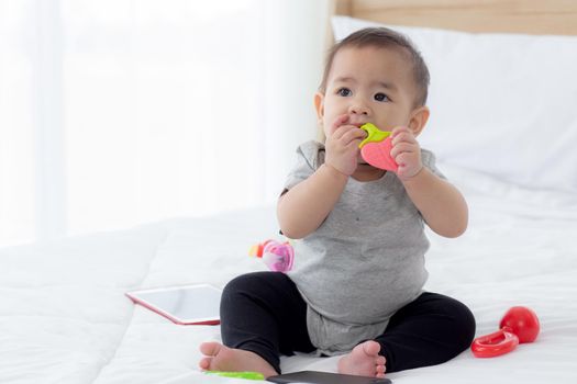Portrait of cute little baby girl sitting with cozy on bed at bedroom, happiness of toddler, newborn 6-11 months with innocence and expression with cheerful, child charm, indoors, one person.