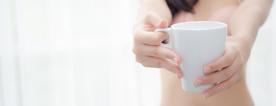 Closeup young asian sexy woman in underwear giving coffee near windows in the morning, girl with seductive figure fit serving beverage is breakfast for relax after wake up, lifestyle concept.