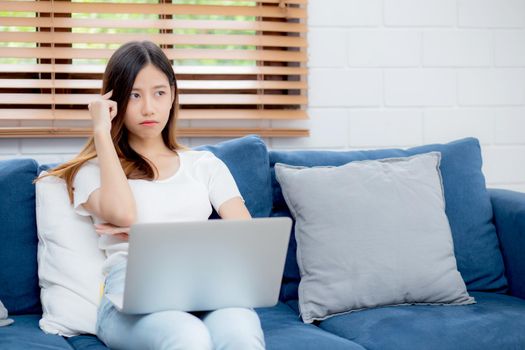 Young asian woman work on laptop computer on sofa at home with frustrated and bored, freelance girl unhappy and tired with unsuccessful, upset from problem, failure and mistake, business concept.
