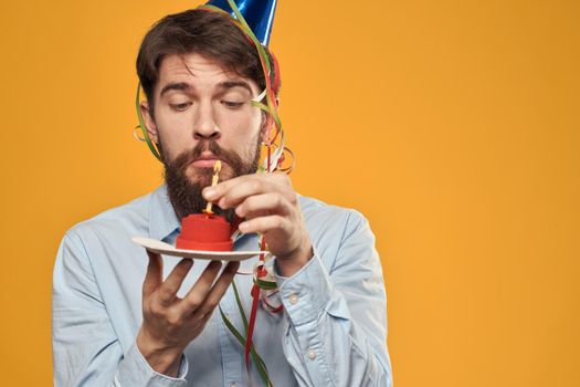 Guy with a cake in a plate on a yellow background holidays candle cropped view. High quality photo