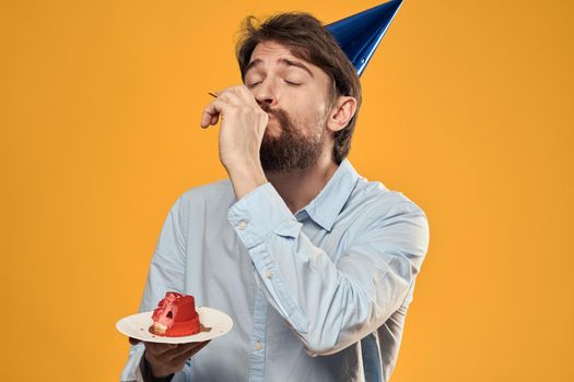 a man with a birthday cake in his hands and in a cap on a yellow background on his birthday. High quality photo
