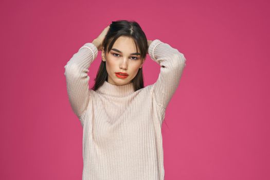 Brunette with long hair red lips cosmetics white sweater pink background cropped view. High quality photo