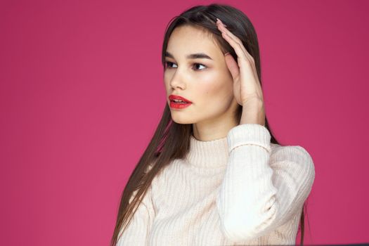Brunette with long hair red lips cosmetics white sweater pink background cropped view. High quality photo
