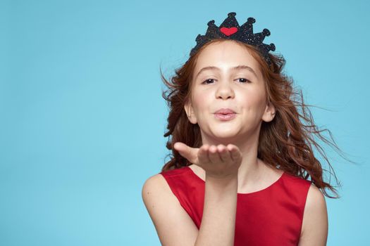 little girl with curly hair with a crown on her head red dress Smile blue background. High quality photo