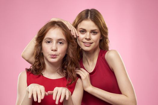 Mom and daughter in red dresses hugs fun grimace childhood joy pink background. High quality photo