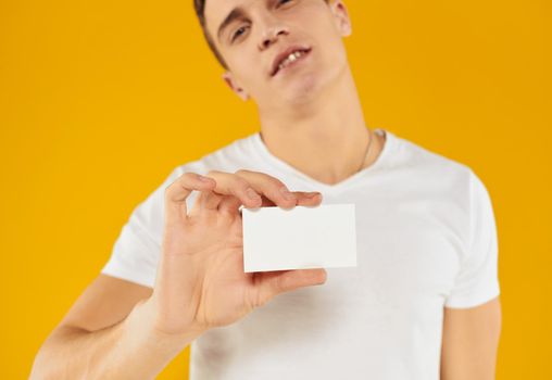 man in white t-shirt showing business card on yellow background cropped view. High quality photo