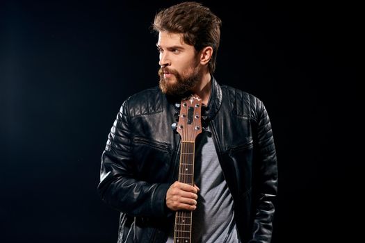 A man with a guitar in his hands leather jacket music performance rock star modern style dark background. High quality photo