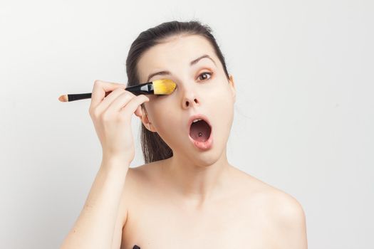 beautiful brunette naked shoulders applying cream brush on face care. High quality photo