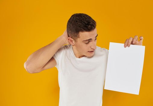 Guy with a white sheet of paper on a yellow background close-up cropped view. High quality photo