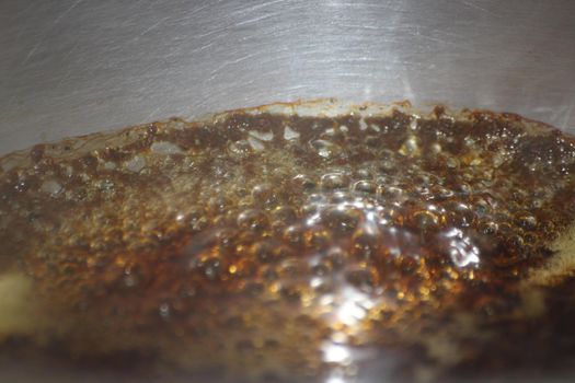 Closeup macro photograph with selective focus of boiling brown water in a metal pan for brewing tea