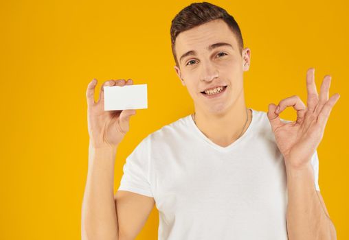 A guy in a white t-shirt shows a credit card on a yellow background cropped view. High quality photo
