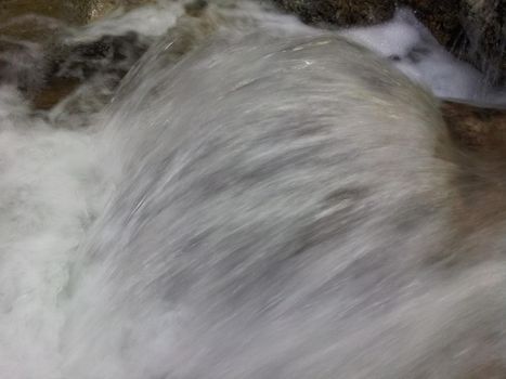 Blurred or unfocused view of flowing water stream in between stones. Flowing water background for texture and advertisements