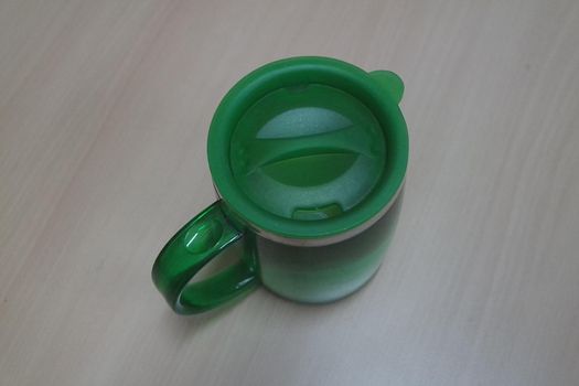 Beautiful coffee green hot mug with green led, placed over white floor. Closeup perspective view of a mug on white desk.
