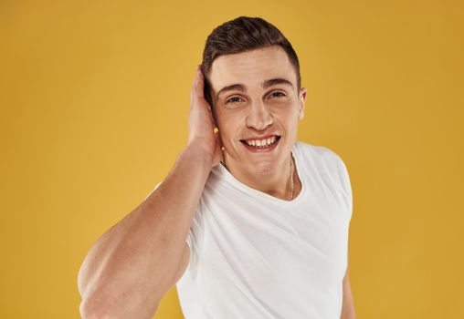 An energetic guy in a white T-shirt touches his head with his hand on a yellow background. High quality photo