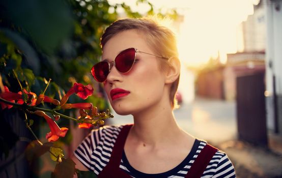 beautiful woman in glasses near red flowers on the street and red sundress striped t-shirt. High quality photo