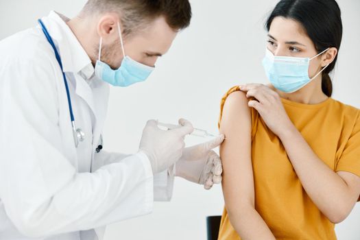 doctor's assistant injections in the shoulder of a woman wearing a medical mask. High quality photo