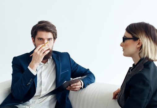 Business man with documents explains something to a young woman Sitting on a sofa indoors. High quality photo