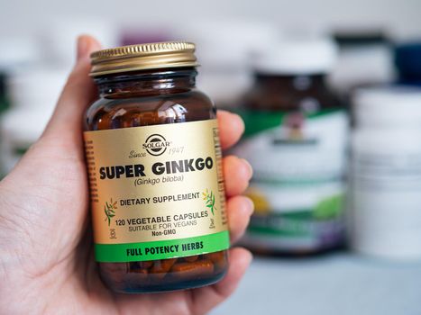 Moscow, Russia - March 09, 2021: Glass jar with Ginkgo capsules in female hand and others nutrition supplements in blurred background. Super Ginkgo by Solgar