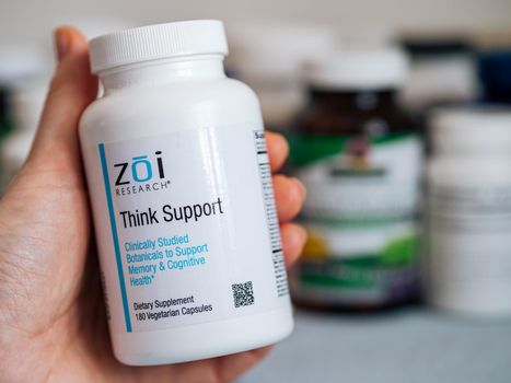 Moscow, Russia - March 09, 2021: Jar Think Support by Zoi Research with capsules in female hand and others nutrition supplements in blurred background. Is blend for memory and cognitive health