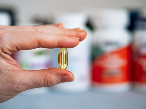 Vitamin D3, Omega or Evening Primrose Oil gel capsule in female hand on blurred dietary supplement jars background. Copy space for text.