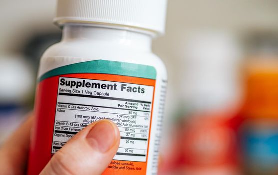 Supplement Facts concept. Close up view of jar with Supplement Facts information in female hand and defocused jars with different dietary supplement on blurred background. Copy space