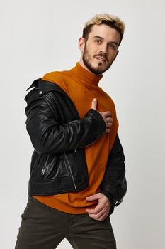 blond guy in a leather jacket with an orange sweater and trousers posing on a light background. High quality photo