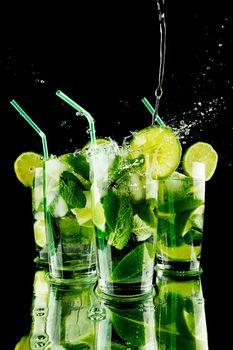 Pouring fresh mojito cocktail in glasses isolated on black background