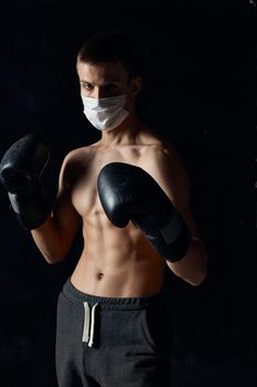 athlete boxing gloves on a black background medical mask on the face naked torso. High quality photo