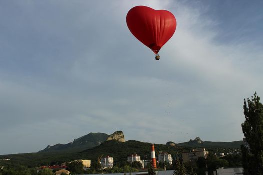 A red-hearted aerostat in the sky above the city. Romantic relationships. High quality photo