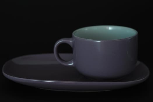 Tea cup with a saucer in the style of Provence on a black background. Purple on black.