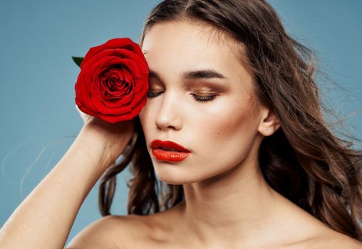 Young woman with red rose near face shadow on eyelids blue background model. High quality photo