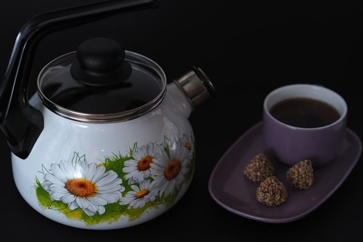 A kettle with a whistle on a black background and a tea pair with candy on a saucer.