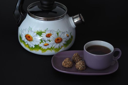 A kettle with a whistle on a black background and a tea pair with candy on a saucer.