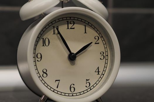 Round clock-alarm white on a gray background, isolated, close-up. High quality photo