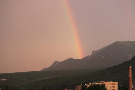 Rainbow over the city at sunset. Mountain landscape with a rainbow. Vertical image.