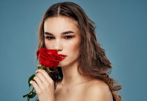Portrait of a beautiful woman with a red flower on a blue background and evening makeup model. High quality photo