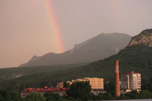 Rainbow over the city at sunset. Mountain landscape with a rainbow. Vertical image.