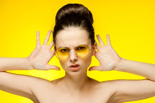 woman with bare shoulders yellow glasses hands near face clear skin. High quality photo