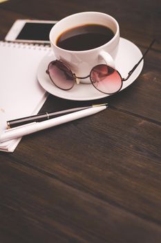 cup of coffee on a saucer wooden table notepad pen office stationery. High quality photo