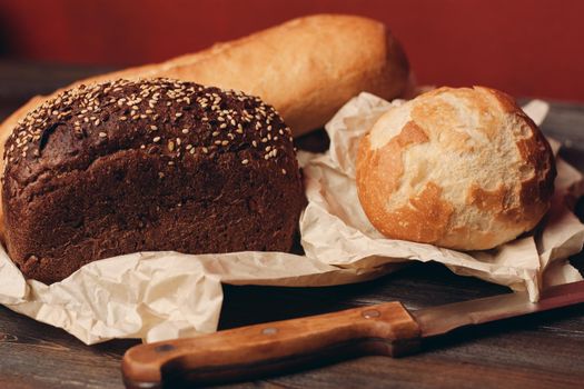 loaf of rye bread and flour products on paper packaging knife on a wooden table and red background. High quality photo