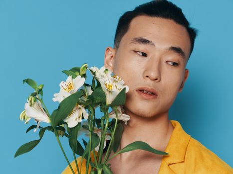 Young man with a bouquet of white flowers on a blue background looks to the side portrait close-up. High quality photo